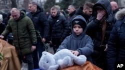 A boy puts a toy on a coffin during a Feb. 5 funeral service in Poltava, Ukraine, for Dmytro Yavorskyi, 37; Sofia Yavorska, 9, and Olena Yavorska 38, who were killed on Feb. 1 by a Russian strike.