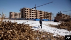 FILE - a Chinese farmer walks past the half completed apartment blocks built to relocate the farmers from Damazizhuang village in northern China's Hebei province. As China tries to protect farmland from development, officials are going after the land underneath farmers' homes instead.
