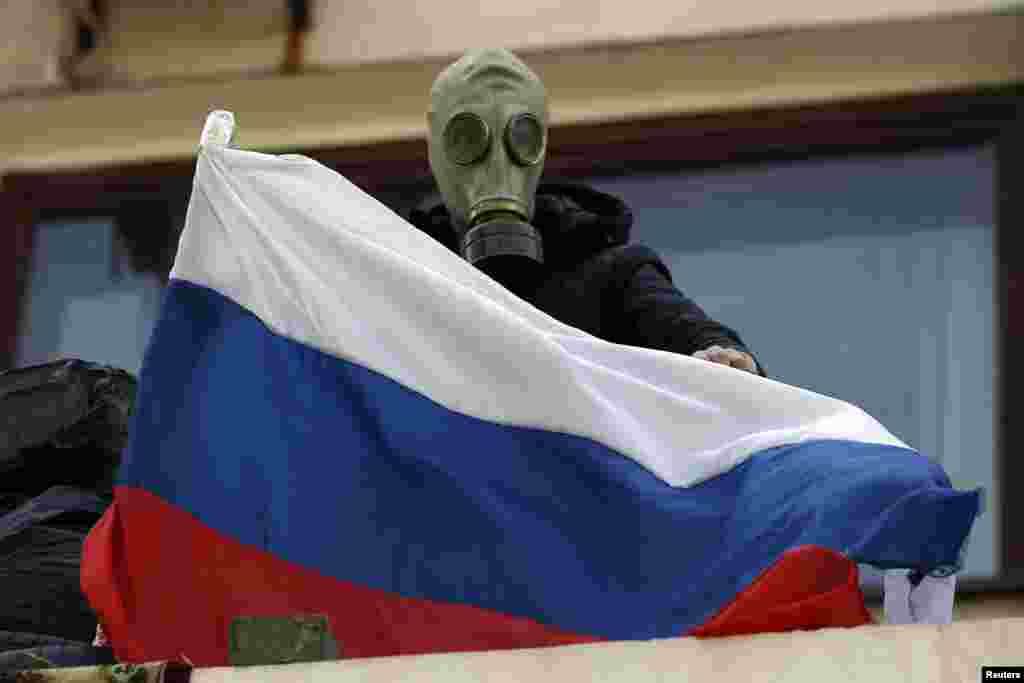 A pro-Russia rebel wearing a gas mask places a Russian flag on the balcony of the city hall in Mariupol, eastern Ukraine, May 7, 2014.