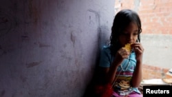 FILE - One of Yennifer Padron and Victor Cordova's daughters eats an arepa in the family room of the house that they share at Petare slum in Caracas, Venezuela, Aug. 21, 2017. 