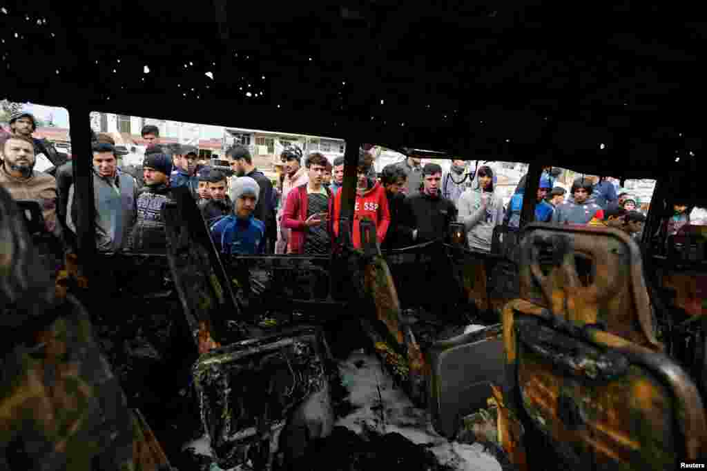 People look at a burned vehicle at the site of car bomb attack in a busy square at Baghdad&#39;s sprawling Sadr City district, Iraq.