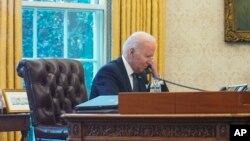 FILE - In this image taken through a window, U.S. President Joe Biden talks on the phone in the Oval Office of the White House in Washington, Dec. 9, 2021. 