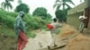 Quelques habitants du quartier d'Abobo traversent une planche sur le système de drainage inondé et le banc de sable construit pour protéger leur maison, à Abidjan, Côte d'Ivoire, 2 juin 1998. 