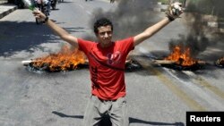 A protester carries stones in one hand and a beer bottle in the other as he kneels in front of burning tires set by protesters in front of Luxor governorate building to protest against the newly-appointed governor, Adel Mohamed al-Khayat in Luxor, Egypt, June 19, 2013. 