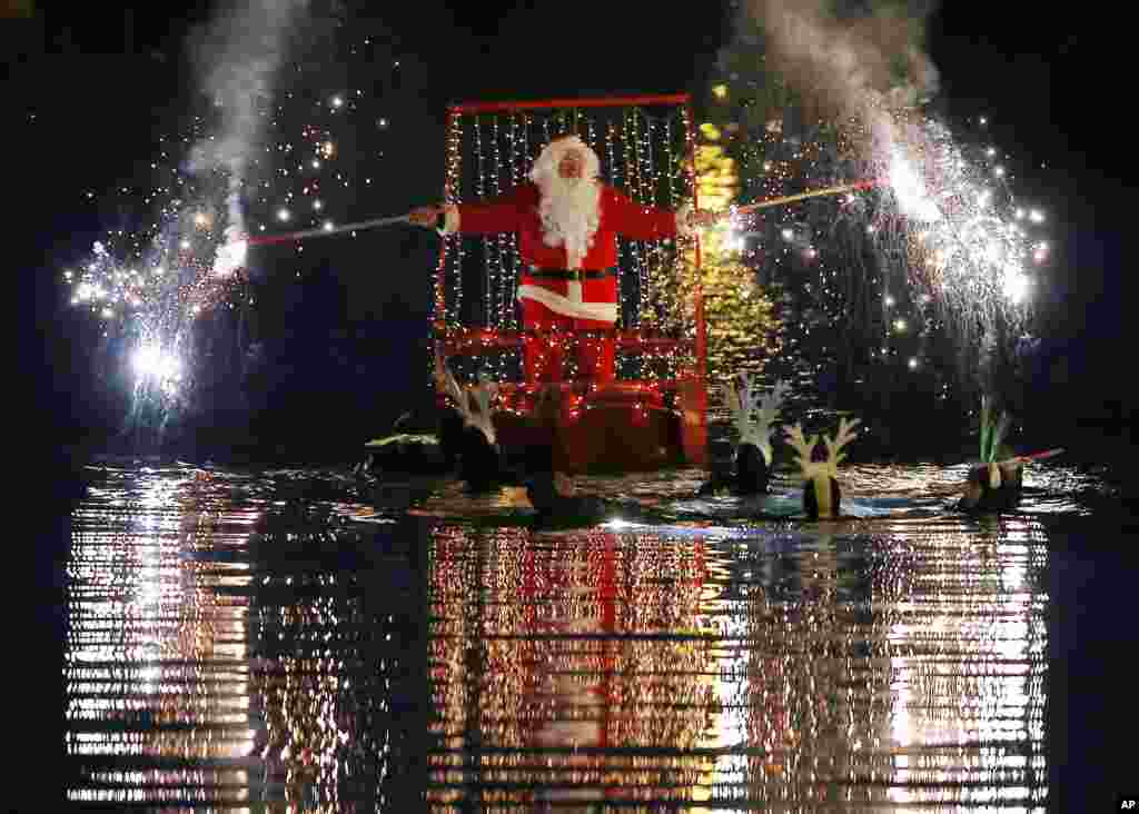 A man dressed as Santa Claus lights flares as he sits on a boat toed by swimmers, in Imperia, near Genoa, Italy.