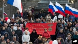 People gather with Russian national and Crimea flags, awaiting the start of a concert with Russian President Vladimir Putin addressing the crowd, in Sevastopol, Crimea, March 14, 2018.