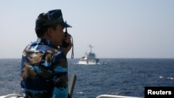 FILE - A Vietnamese coast guard officer speaks on a radio as he monitors a Chinese vessel (top) in the South China Sea, about 210 km off Vietnam's shore, May 15, 2014. Chinese incursions into Vietnamese waters have increased since early May 2023.