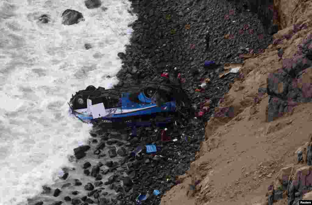 Rescue workers stand at the scene after a bus crashed with a truck and careened off a cliff along a sharply curving highway north of Lima, Peru.