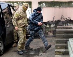 FILE - A Ukrainian sailor, right, is escorted by a Russian FSB officer to a courtroom in Simferopol, Crimea, Nov. 27, 2018. Russians captured Ukrainian seamen and their vessels two days earlier as they were about to transit the Kerch Strait.