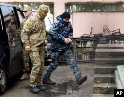 FILE - A Ukrainian sailor, right, is escorted by a Russian FSB officer to a courtroom in Simferopol, Crimea, Nov. 27, 2018. Russians captured Ukrainian seamen and their vessels two days earlier as they were about to transit the Kerch Strait.