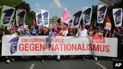 People walk with posters reading: 'Elect a Europe for all' and 'Your choice - May 26.' behind a banner reading: 'A Europe for all; against nationalism,' as they attend a demonstration in Berlin, Germany, May 19, 2019.