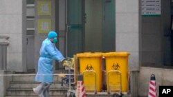 A staff member moves bio-waste containers past the entrance of the Wuhan Medical Treatment Center, where some people infected with a new virus are being treated, in Wuhan, China, Jan. 22, 2020. 