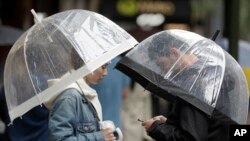 A couple shelter under an umbrellas as rain falls in Sydney, Feb. 7, 2020, while the Bureau of Meteorology issued severe weather warning along the New South Wales state coast. The rain comes as a slight relief for some areas dealing with wildfires.