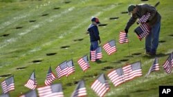 Joseph Manning, right, of Raynham, Mass., and his son Joey, 6, a Cub Scout, place U.S. flags at the graves of deceased veterans at the National Cemetery in Bourne, Mass., Saturday, Nov. 10, 2012. 