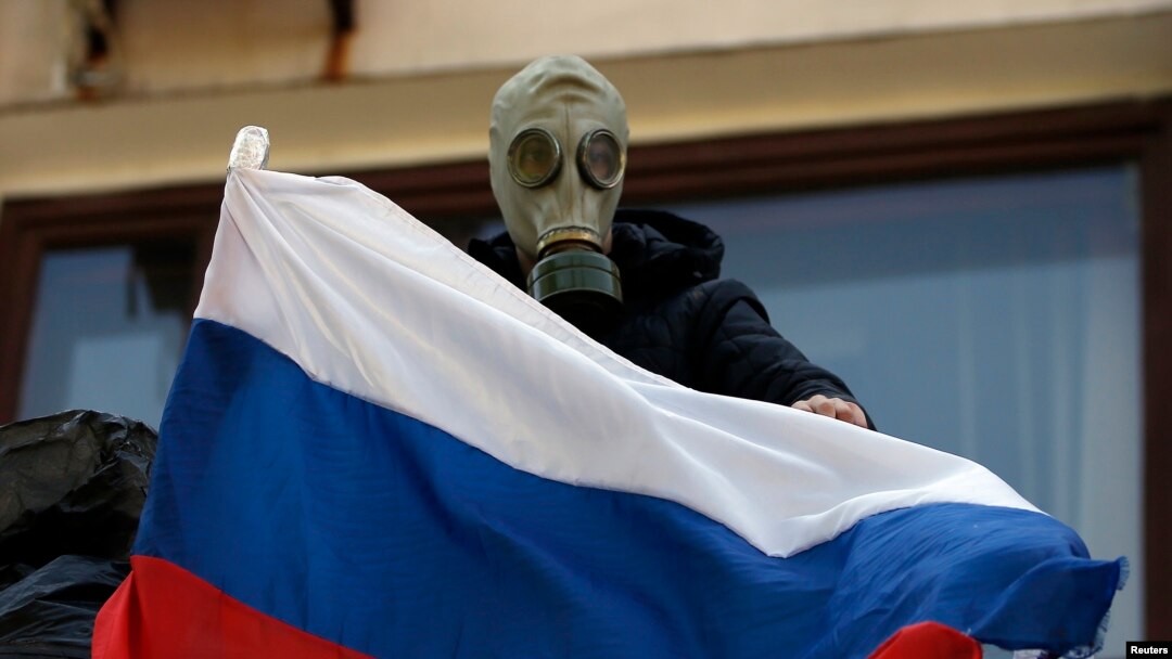 A pro-Russia rebel wearing a gas mask places a Russian flag on the balcony of the city hall in Mariupol, eastern Ukraine May 7, 2014. 