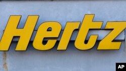 In this Nov. 28, 2017 photo a Hertz rental car logo rests on the front of a Hertz location, in Boston. Car rental company Hertz is ordering 100,000 electric vehicles from Tesla. 