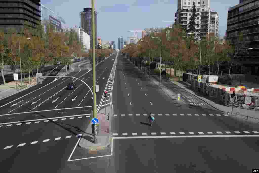 A woman crosses the usually busy La Castellana avenue in Madrid, Spain. France and Spain are the latest European nations to severely curtail people&#39;s movements to fight the coronavirus pandemic.