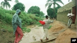 Quelques habitants du quartier d'Abobo traversent une planche sur le système de drainage inondé et le banc de sable construit pour protéger leur maison, à Abidjan, Côte d'Ivoire, 2 juin 1998. 