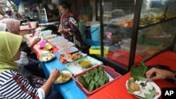 Customers eat nasi uduk, which is Indonesian style steamed rice cooked in coconut milk dish, at street food stall in Jakarta, Indonesia. Tuesday, April 3, 2018. Some Indonesians believe that a woman who eats chicken wings will have a hard time finding a husband. Others claim that by eating the fruit of the pineapple tree, a woman reduces her chances of having a child. (AP Photo/Tatan Syuflana)