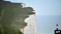 People walk along the cliff-top above the lighthouse at Beachy Head near Eastbourne on the south coast of England following an easing of lockdown rules in England during the COVID-19 pandemic.