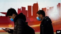 People wearing face masks to help curb the spread of the coronavirus walk by a moral depicting China's skyscrapers along a street in Beijing, Sunday, Dec. 6, 2020. Provincial governments across China are placing orders for experimental, domestically…