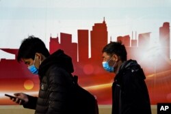 People wearing face masks to help curb the spread of the coronavirus walk by a mural depicting China's skyscrapers along a street in Beijing, Dec. 6, 2020.