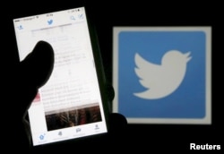 FILE - A man reads tweets on his phone in front of a displayed Twitter logo, March 10, 2016.