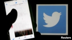 FILE - A man reads tweets on his phone in front of a displayed Twitter logo in Bordeaux, southwestern France, March 10, 2016. 