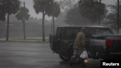 Un homme marche sous la pluie avec des sacs de provisions alors que l'ouragan Helene s'intensifie à Apalachicola, Floride, États-Unis, le 26 septembre 2024. 