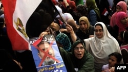 Opposition protesters shout slogans and show a defaced poster of their president as they gather in thousands at the Presidential Palace to protest against Egyptian President Mohamed Morsi and the Muslim Brotherhood in Cairo, July 2, 2013.