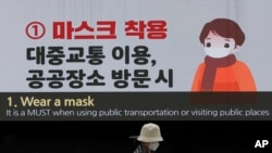 A woman wearing a face mask passes by a screen showing precautions against the coronavirus at the Dongdaemun Design Plaza in Seoul, South Korea, April 19, 2020. 