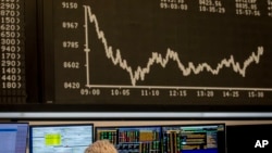 FILE - A broker watches her screens under the curve of the German stock index DAX in Frankfurt, Germany.