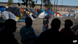 FILE - Men discuss rumors of other migrants who successfully snuck into the U.S. in a tent camp outside the closed Benito Juarez sports complex, in Tijuana, Mexico, Dec. 7, 2018.