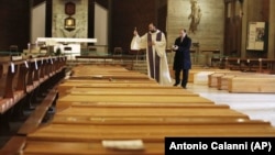 FILE - In this March 28, 2020, file photo, Don Marcello Crotti, left, blesses the coffins with Don Mario Carminati in the San Giuseppe church in Seriate, Italy. (AP Photo/Antonio Calanni, File)