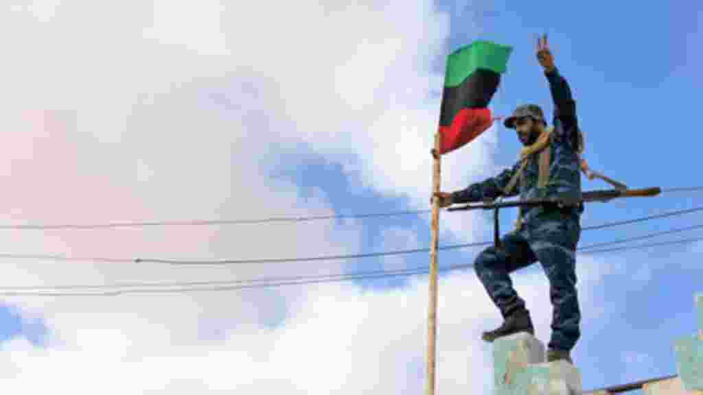 A Libyan soldier who has joined the opposition hoists the pre-Gadhafi era flag, February 23, 2011. (VOA Photo/E. Arrott)