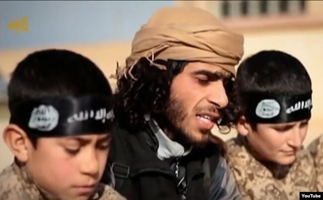 FILE - А screen grab from an Islamic State propaganda video shows an Islamic State recruiter with two child soldiers at an unknown location. Experts warn that not enough thought is being given about what to do with so-called