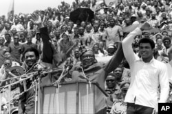 FILE - Zaire's President Mobutu Sese Seko, center, raises the arms of heavyweight champion George Foreman, left, and Muhammad Ali, right, in Kinshasa, Zaire, Sept. 22, 1974. The two boxing greats faced off in the legendary "Rumble in the Jungle" fight in Kinshasa, Oct. 29, 1974.