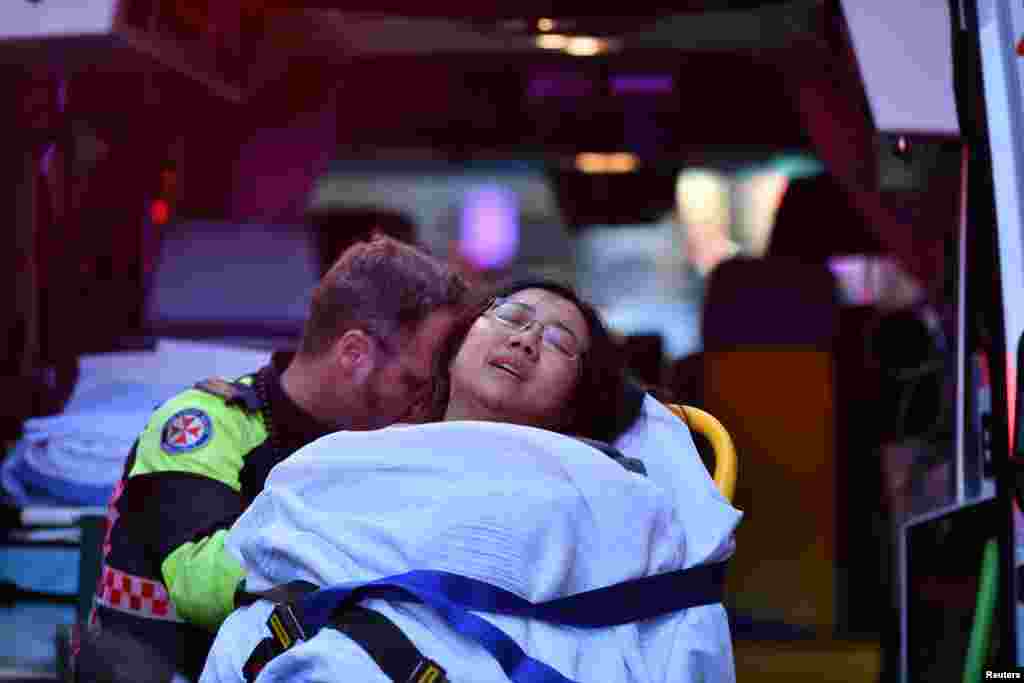 A woman is taken by ambulance to a hospital as police officers investigate the scene following reports of a stabbing in Sydney, Australia.