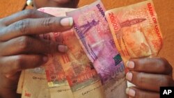 FILE — A Ugandan businesswoman counts Shilling banknotes in Kampala, Feb. 27, 2014. 