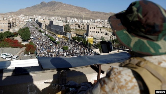 A Houthi militant sits guard on the roof of a building overlooking fellow Houthis rallying to denounce the rapid devaluation of the Yemeni Rial in Sanaa, Yemen, Oct. 5, 2018.