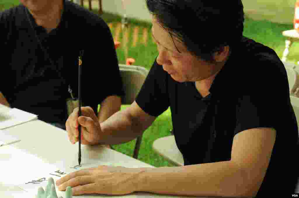 Beijing artist Yang Guangxin patiently paints a visitor’s name in Chinese calligraphy at the Smithsonian Folklife Festival in Washington, June 25, 2014. (Regina Catipon/VOA)