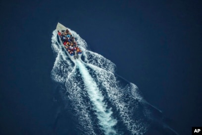 FILE - Migrants navigate on an overcrowded wooden boat in the Central Mediterranean Sea between North Africa and the Italian island of Lampedusa, Oct. 2, 2021, as seen from aboard the humanitarian aircraft Seabird.