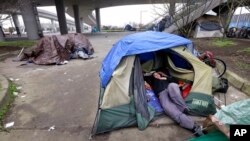 FILE - A man lies in a tent with others camped nearby, under and near an overpass in Seattle, Feb. 9, 2016. Microsoft pledged $500 million to address homelessness and develop affordable housing in response to the Seattle region's widening affordability gap.