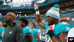 Miami Dolphins defensive end Robert Quinn raises his right fist during the singing of the National Anthem, before the start of an NFL preseason football game against the Tampa Bay Buccaneers, Aug. 9, 2018 in Miami Gardens, Fla.