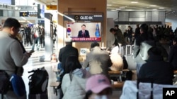 12일 한국 서울역에서 시민들이 윤석열 대통령의 대국민담화 보도를 시청하고 있다.