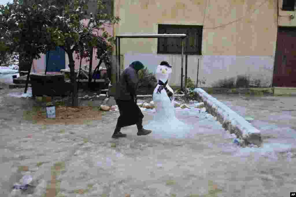 A Palestinian woman walks by a snowman in the West Bank town of Nablus, Dec. 13, 2013.