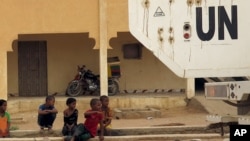 Des enfants assis sur une rue à côté d'un véhicule de l'ONU qui passe à Kidal, Mali, 23 juillet 2015.