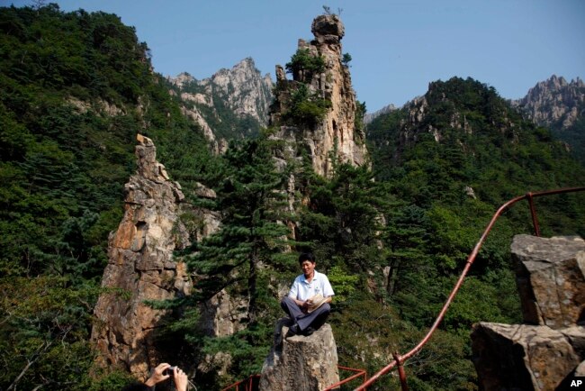 ຜູ້ນ່ຳທ່ຽວເກົາຫີ້ຼເໜື້ອຄົນນຶ່ງ ນັ່ງຖ່າຍຮູບ ຢູ່ພູເກີນກັງ ບ່ອນຕາກອາກາດ ໃນເກົາຫຼີເໜືອ.