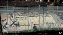 A man walks past the smoldering remains of burnt out buildings at Sydney's Villawood Detention Centre, April 21, 2011