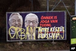 A billboard from a campaign of the Hungarian government showing EU Commission President Jean-Claude Juncker and Hungarian-American financier George Soros with the caption "You, too, have a right to know what Brussels is preparing to do" is displayed at a street in Budapest, Hungary, Feb. 26, 2019. The Hungarian government claims that EU leaders like Juncker, backed by Soros, want to bring mass migration into Europe. The billboard has been sprayed with graffiti saying "Orban thief," in reference to Hungarian Prime Minister Viktor Orban.